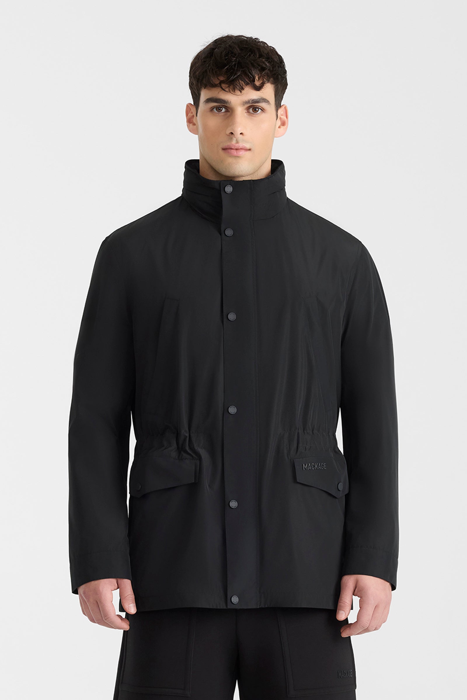 Man wearing a black medium-length rain jacket, and shorts on a white background.