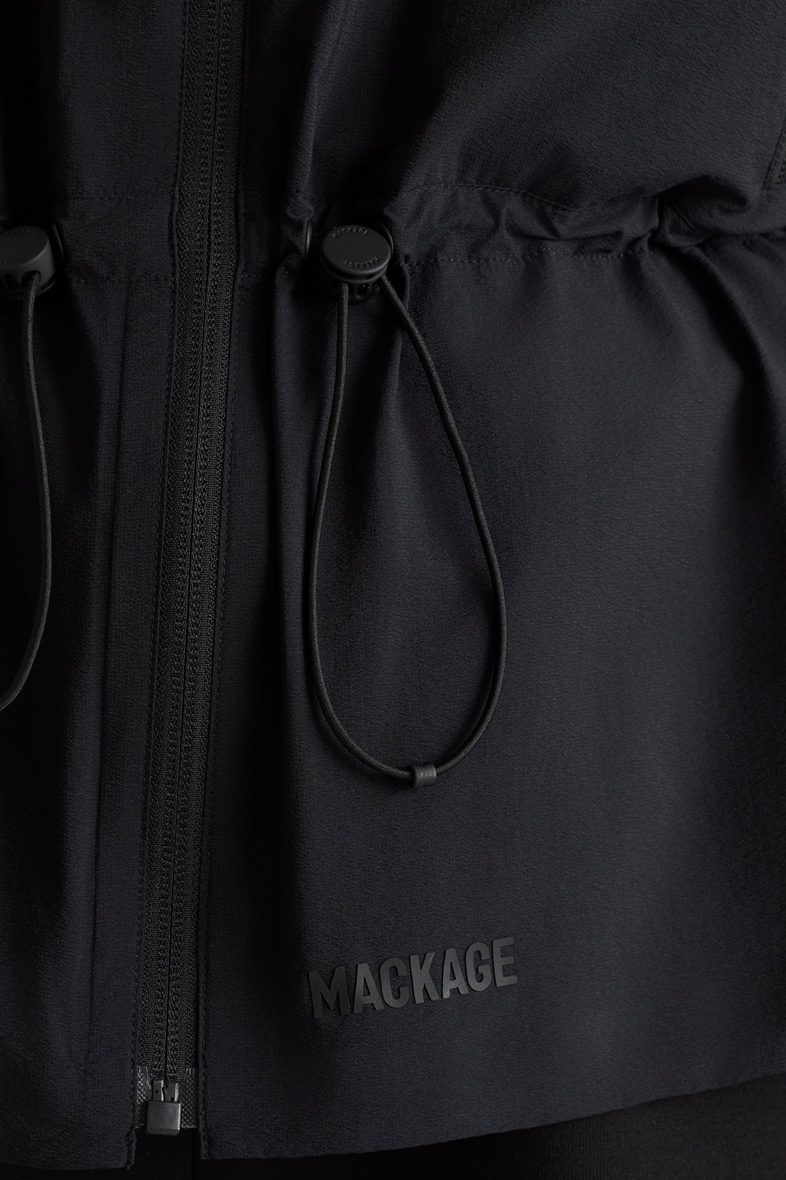 Close-up of a black jacket with a drawstring and 'Mackage' logo.