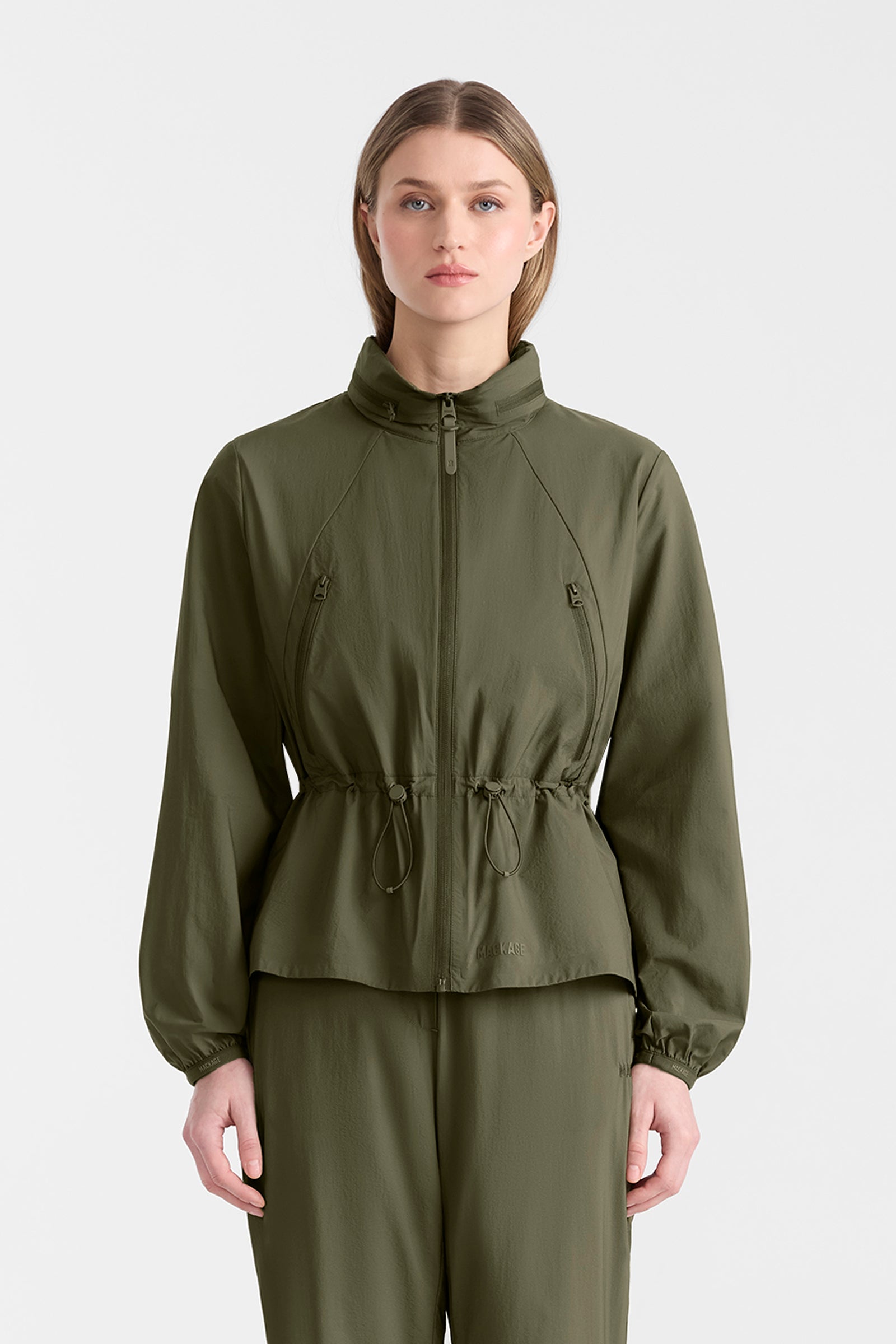 Woman wearing a light military jacket and pants on a white background