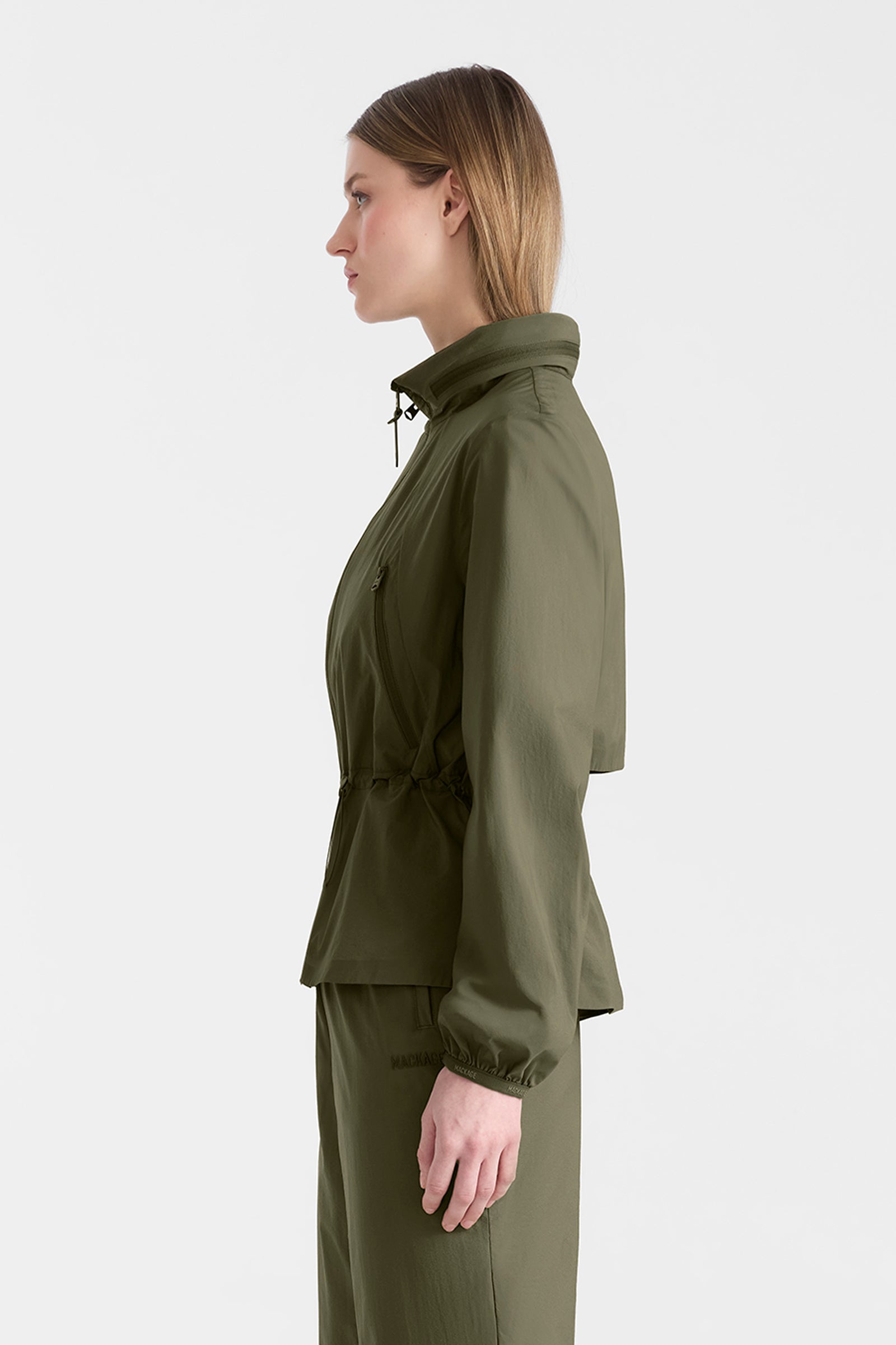 Woman wearing a light military jacket and pants on a white background