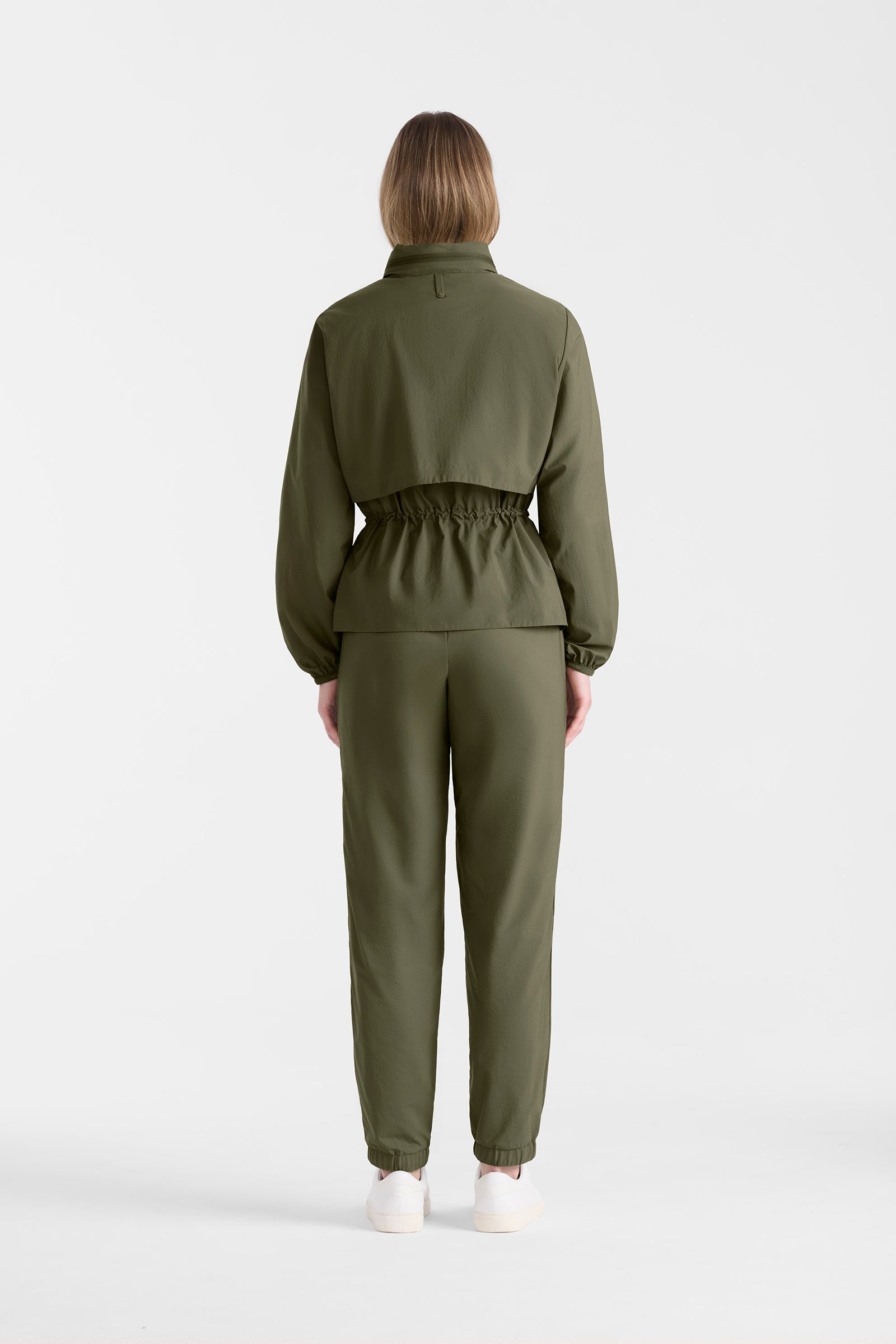 Woman wearing a light military jacket and pants on a white background