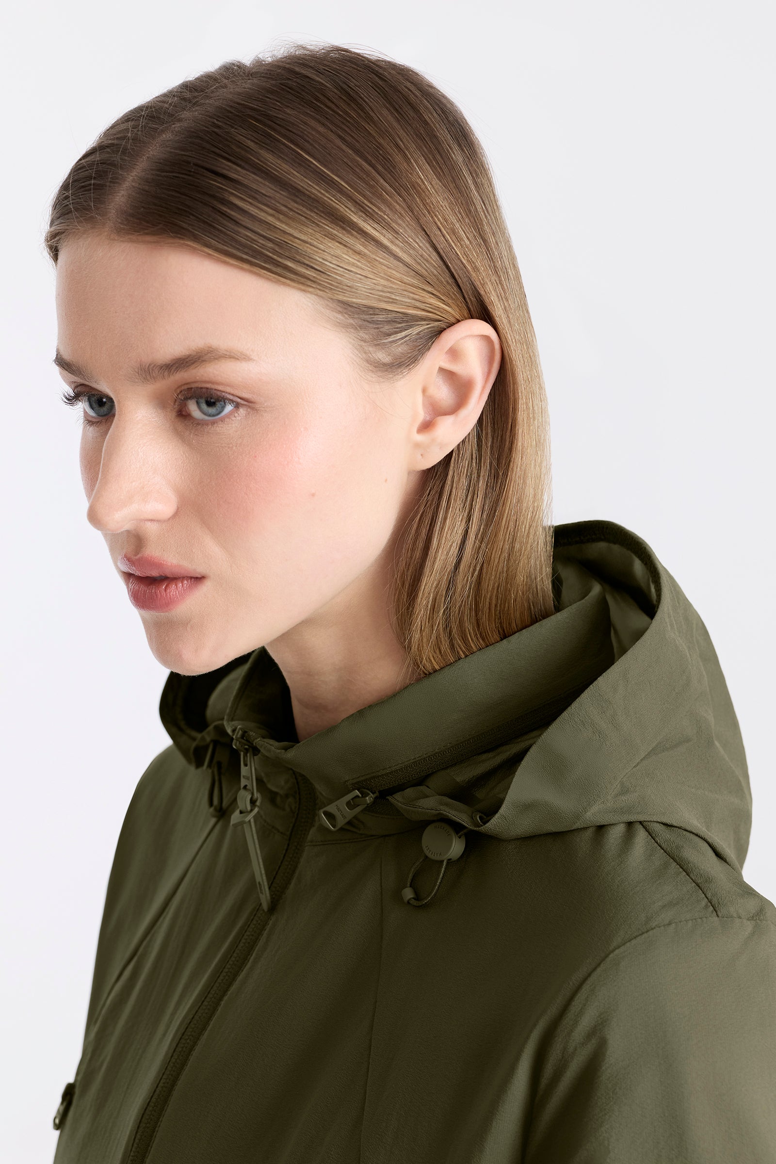Woman wearing a light military jacket with a hood on a white background