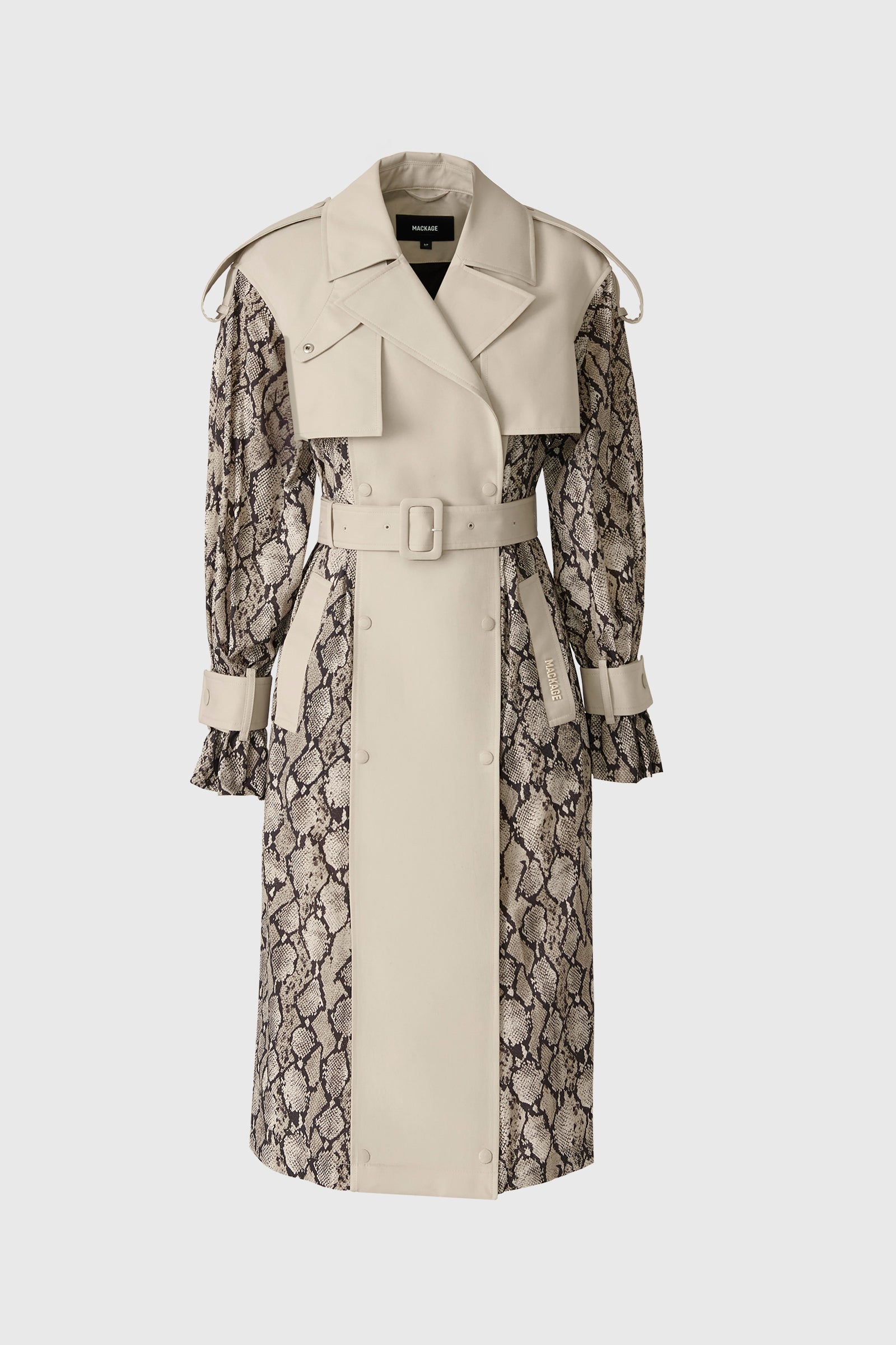 Woman wearing a snake-taupe-patterned trench coat standing beside a white off-road vehicle in a desert landscape.