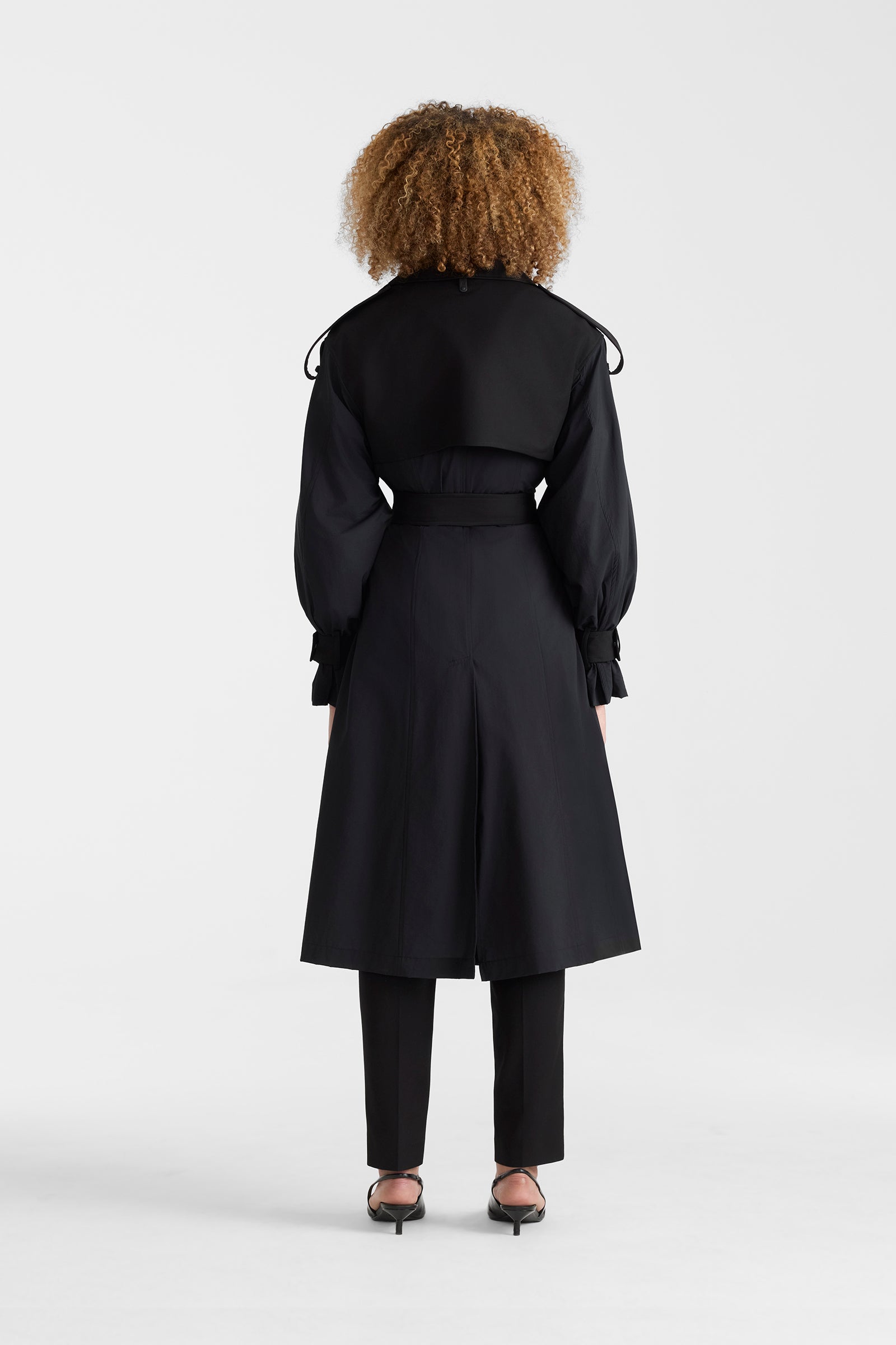 Woman wearing a black lightweight trench coat on a white background.