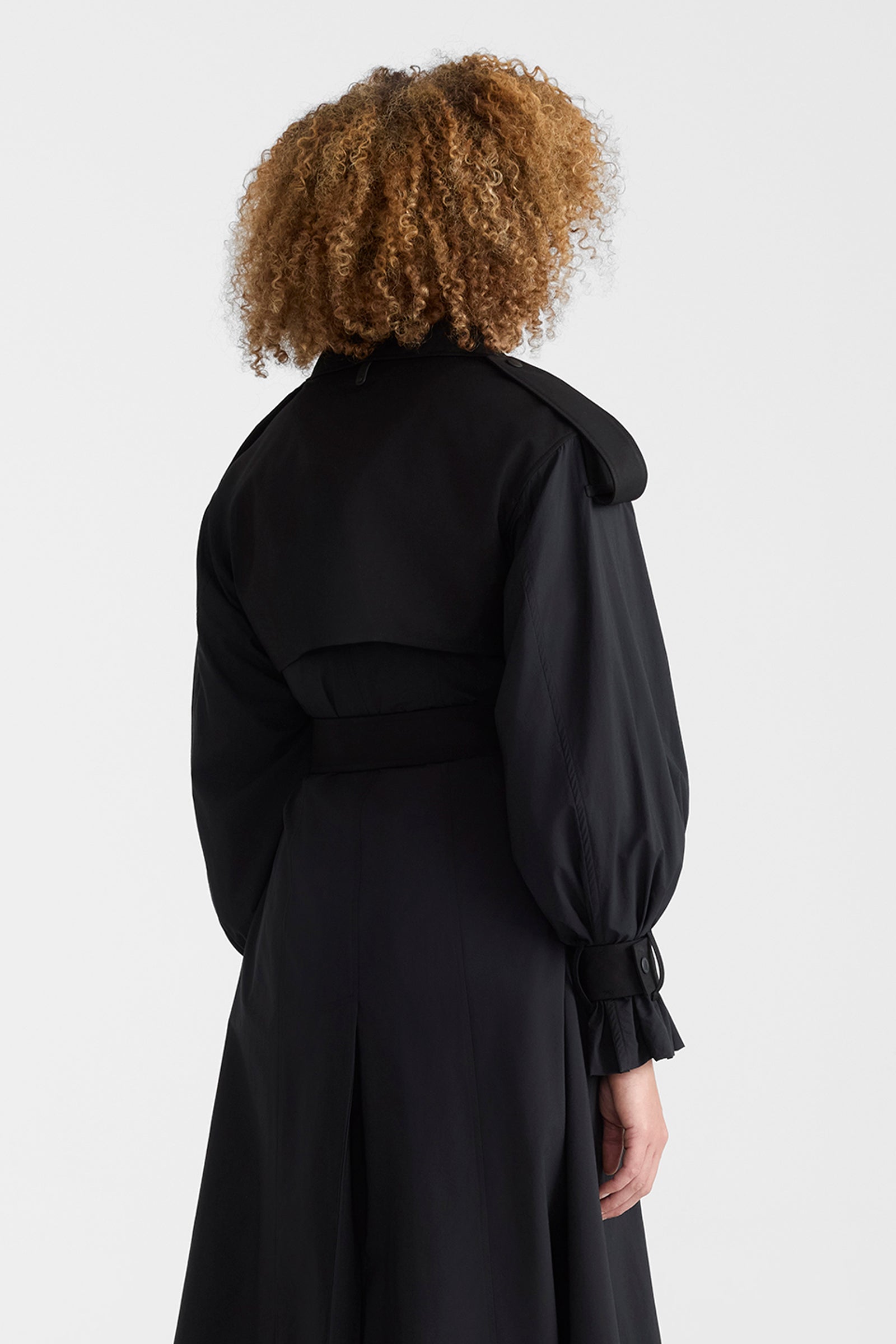 Woman wearing a black lightweight trench coat on a white background.