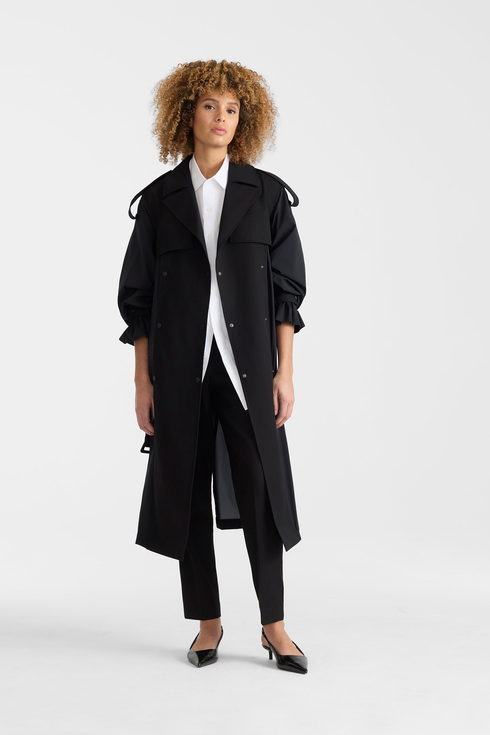 Woman wearing a black lightweight trench coat on a white background.