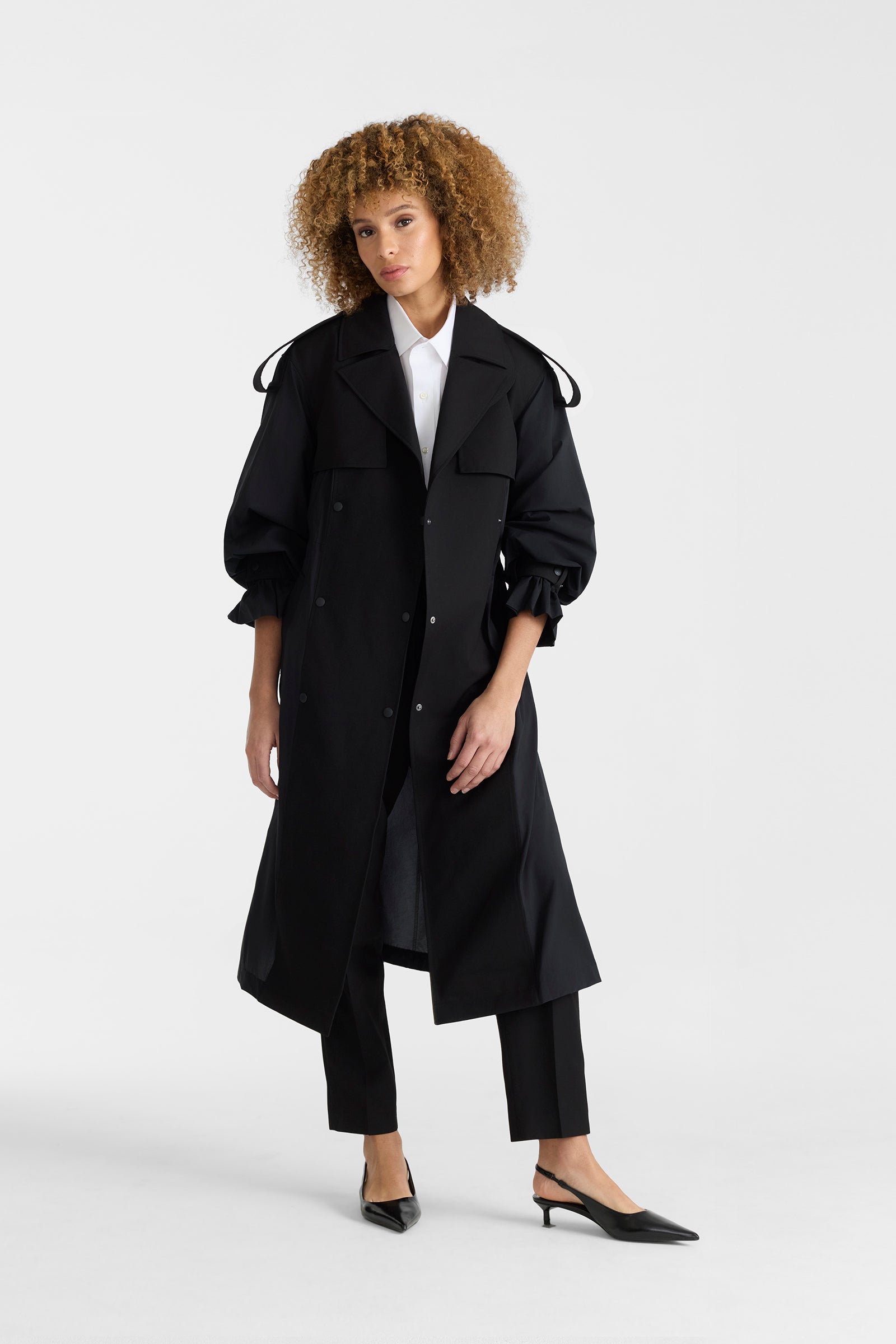 Woman wearing a black lightweight trench coat on a white background.