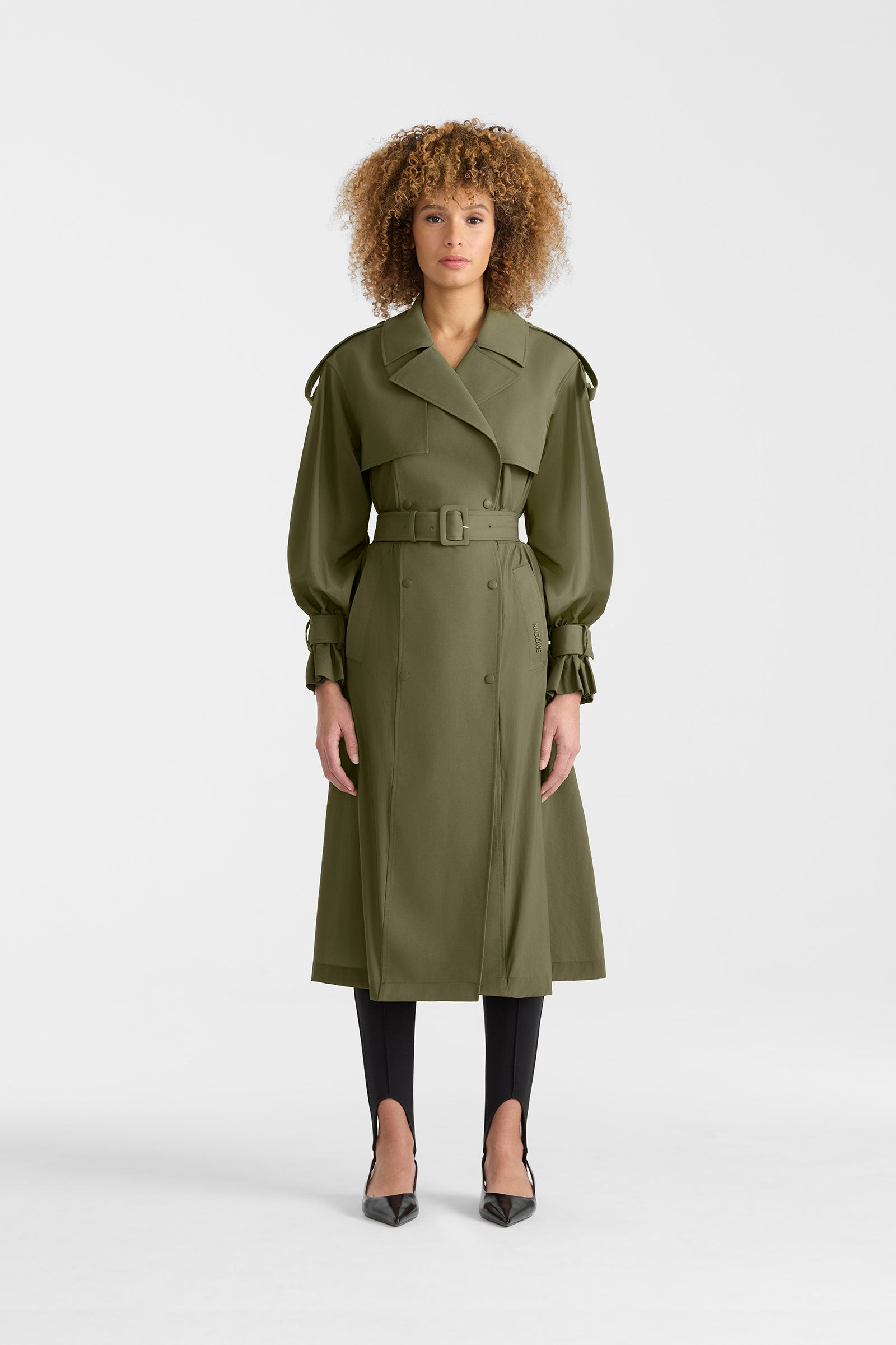 Woman wearing a lightweight trench coat in light military colour on a white background.