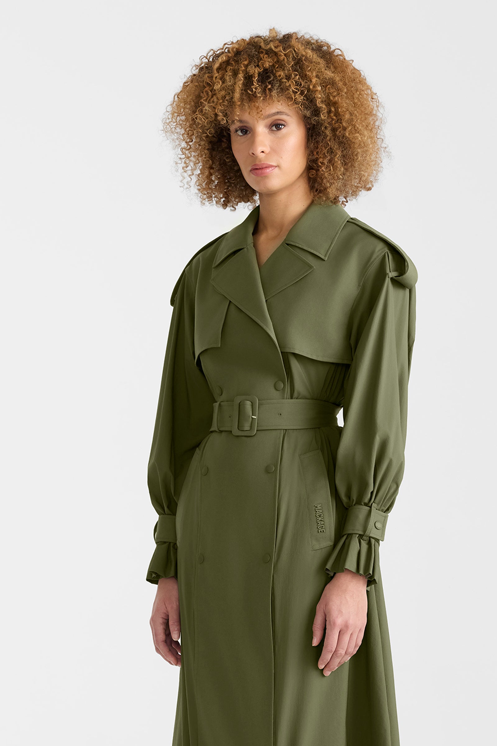 Woman wearing a lightweight trench coat in light military colour on a white background.
