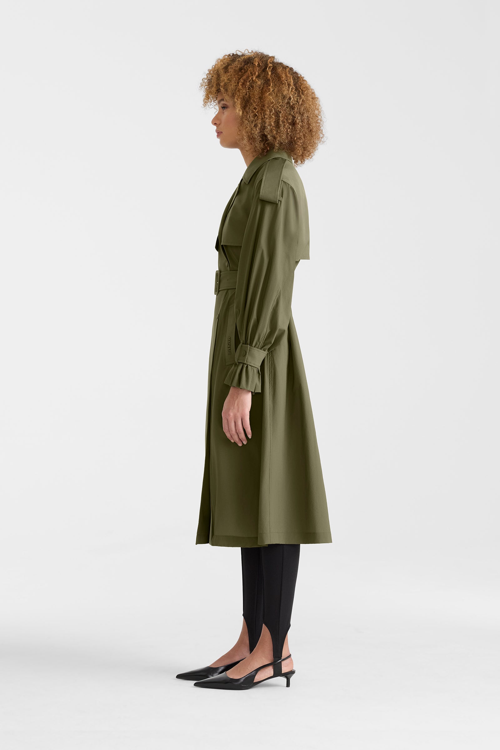 Woman wearing a lightweight trench coat in light military colour on a white background.