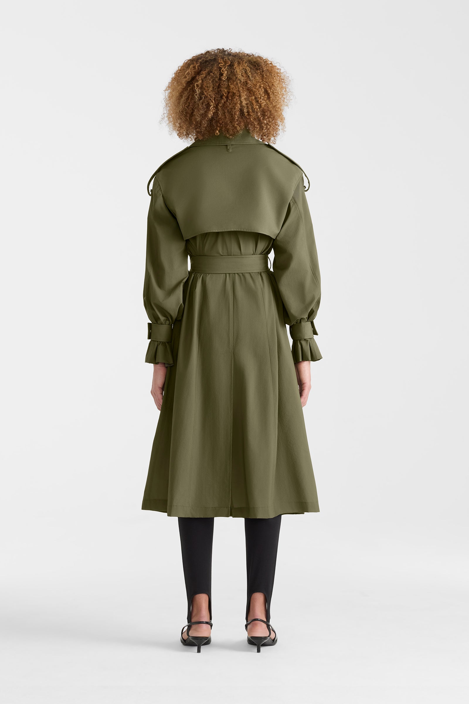 Woman wearing a lightweight trench coat in light military colour on a white background.