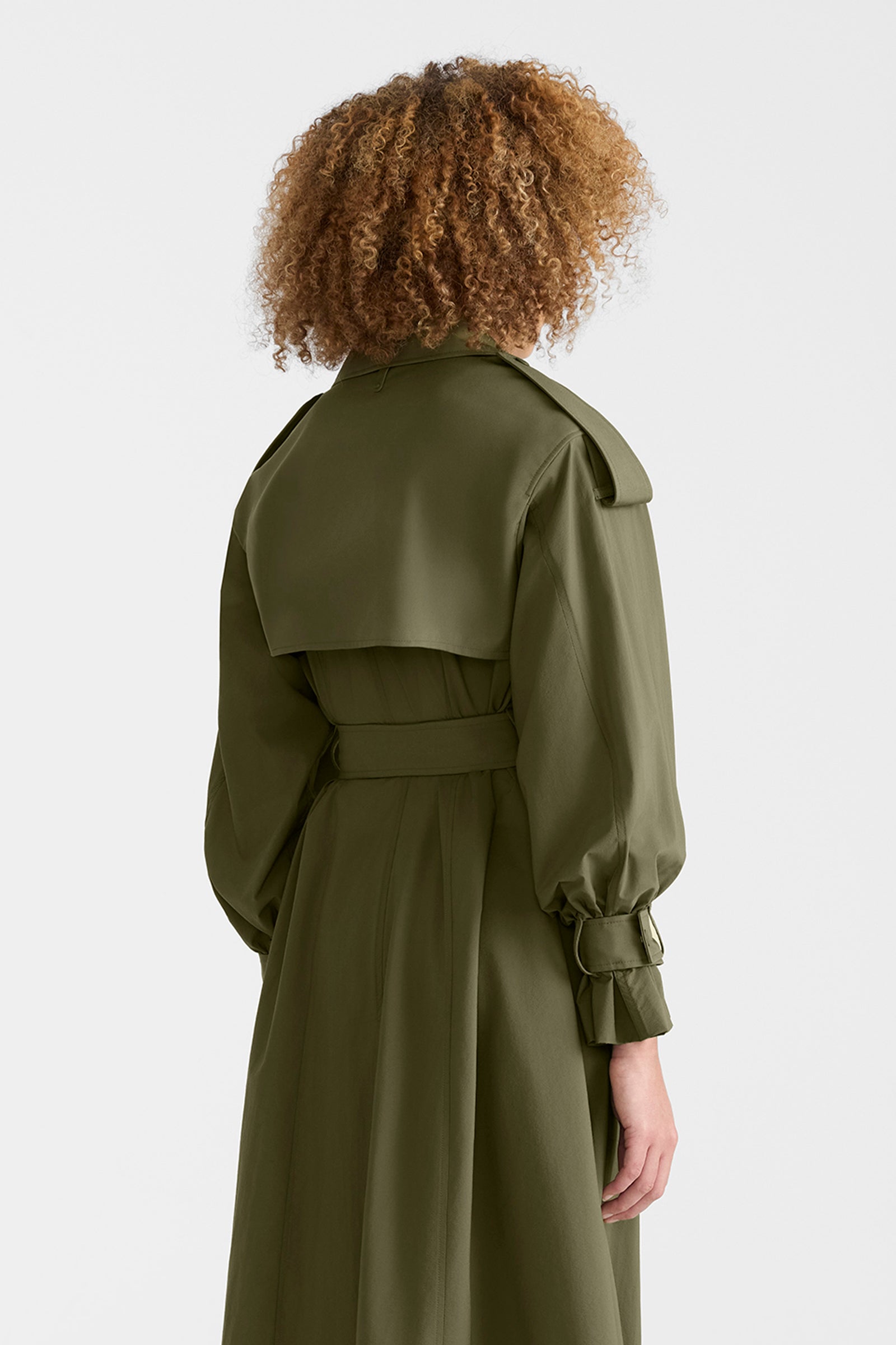 Woman wearing a lightweight trench coat in light military colour on a white background.