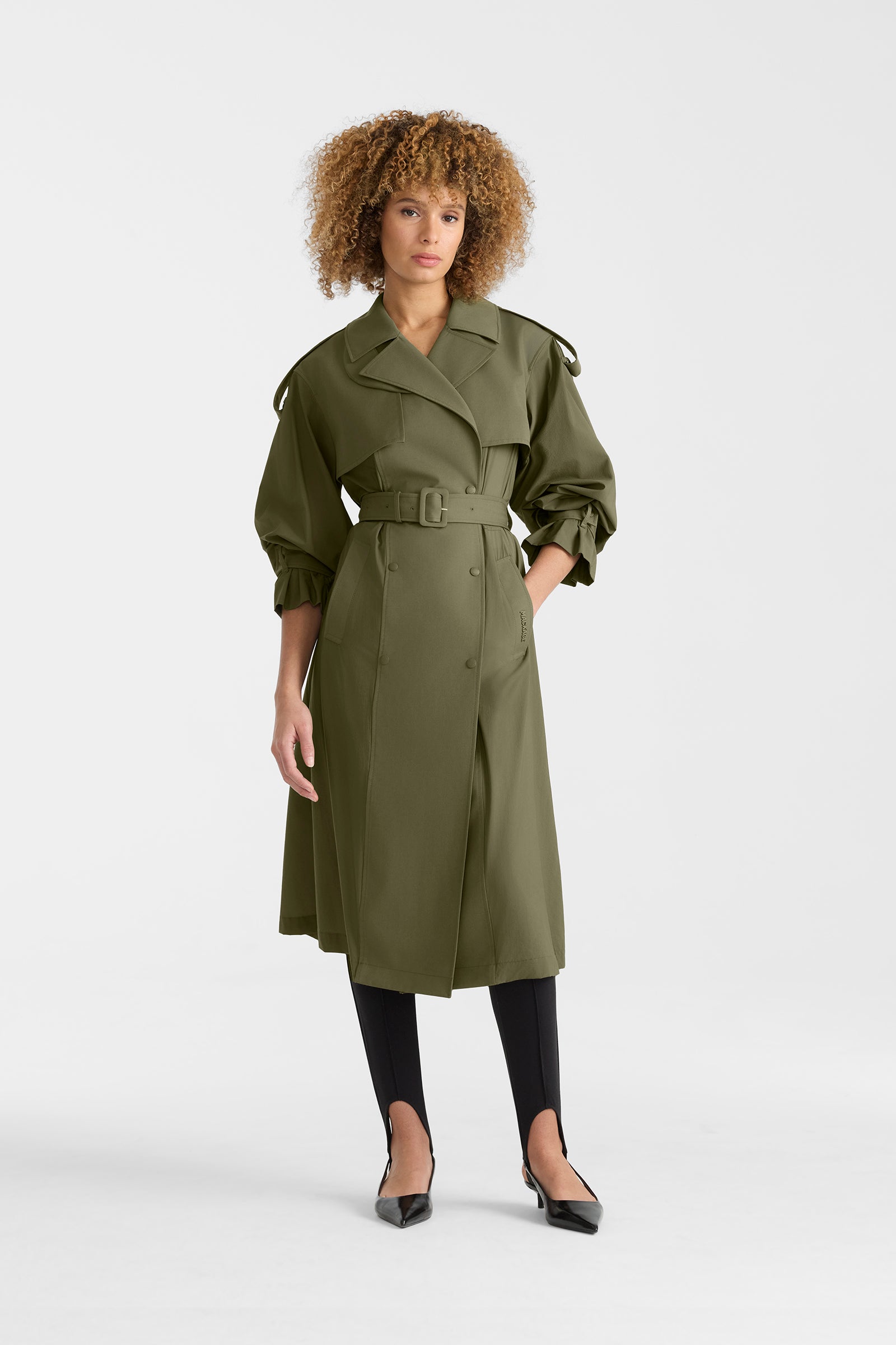 Woman wearing a lightweight trench coat in light military colour on a white background.
