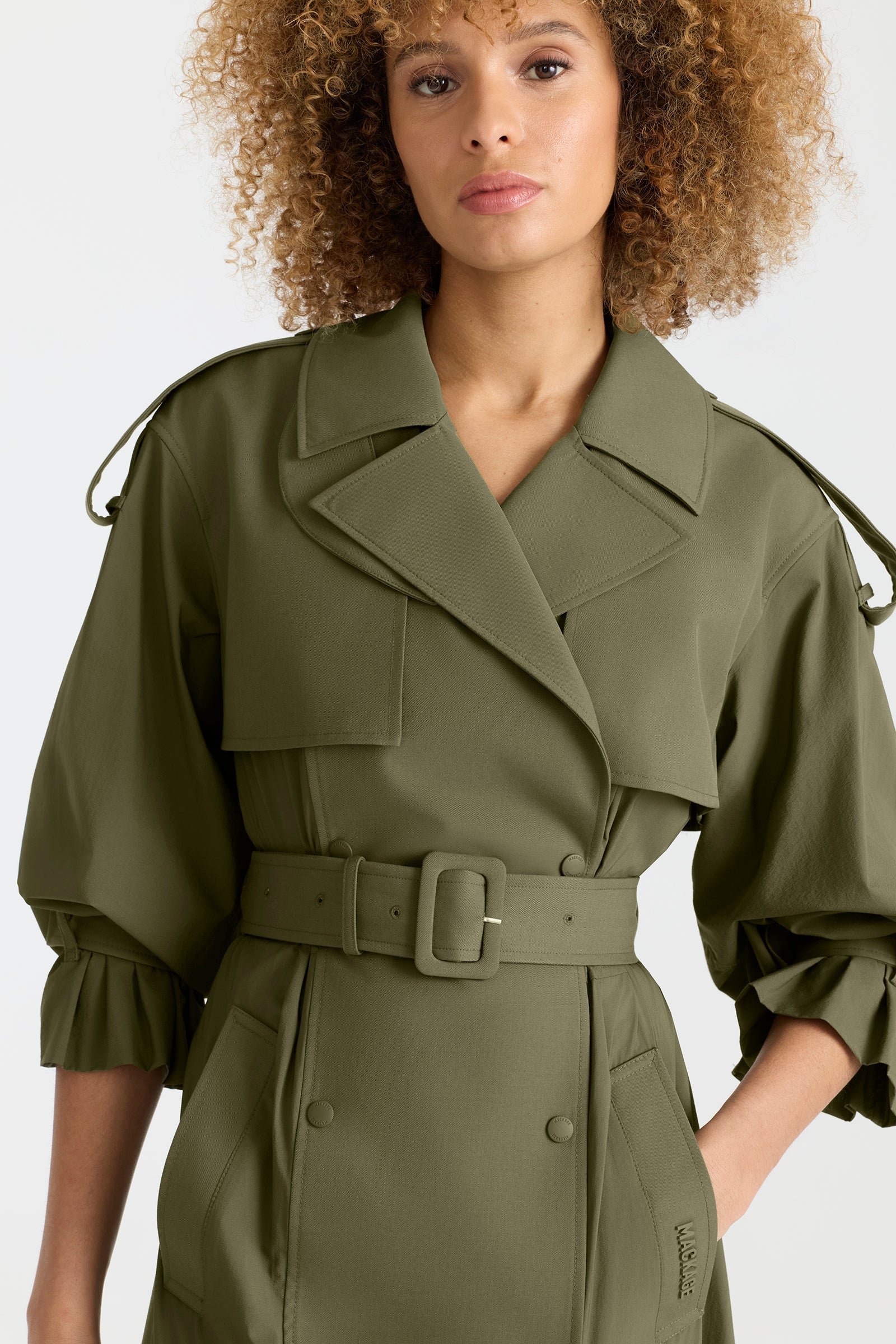 Woman wearing a lightweight trench coat in light military colour on a white background.