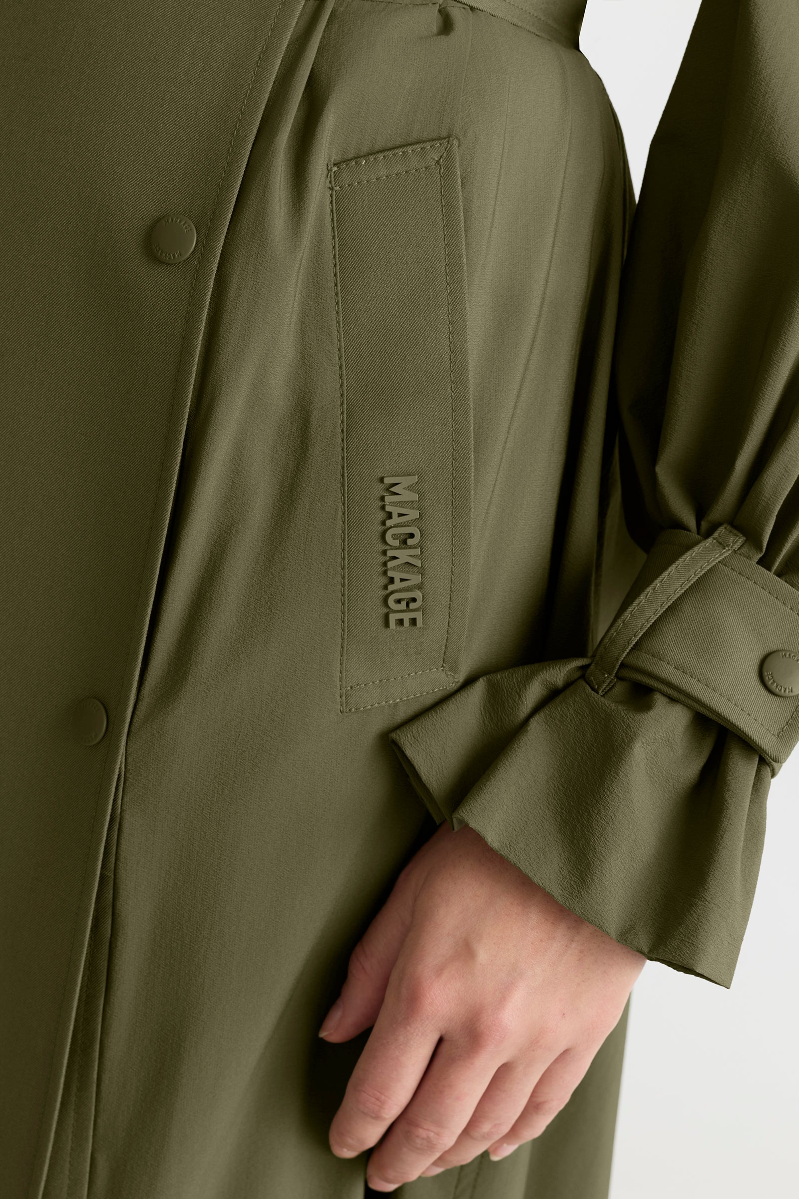 Close-up coat in light military colour with a visible MACKAGE logo on a neutral background.
